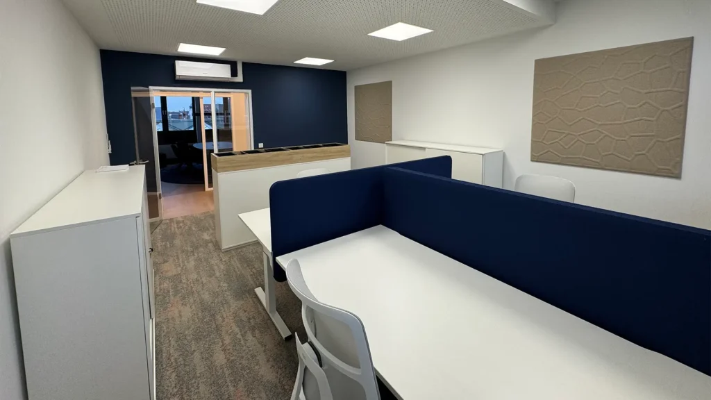 Arbeitsbereich mit Einzelarbeitsplätzen, weißen Schreibtischen, blauen Akustik-Trennwänden und Stauraummöbeln.