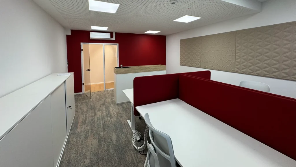 Arbeitsbereich mit identischer Raumaufteilung, roten Akustik-Trennwänden und hellem Bodenbelag.