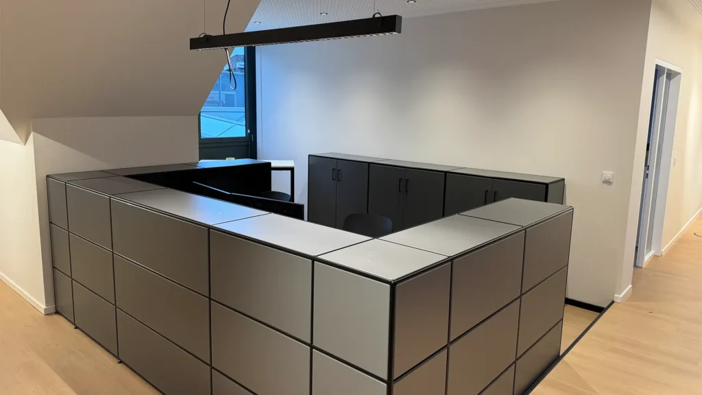 Empfangs- oder Arbeitsbereich mit U-förmigem Tresen aus grauen Modulen und moderner Pendelleuchte.