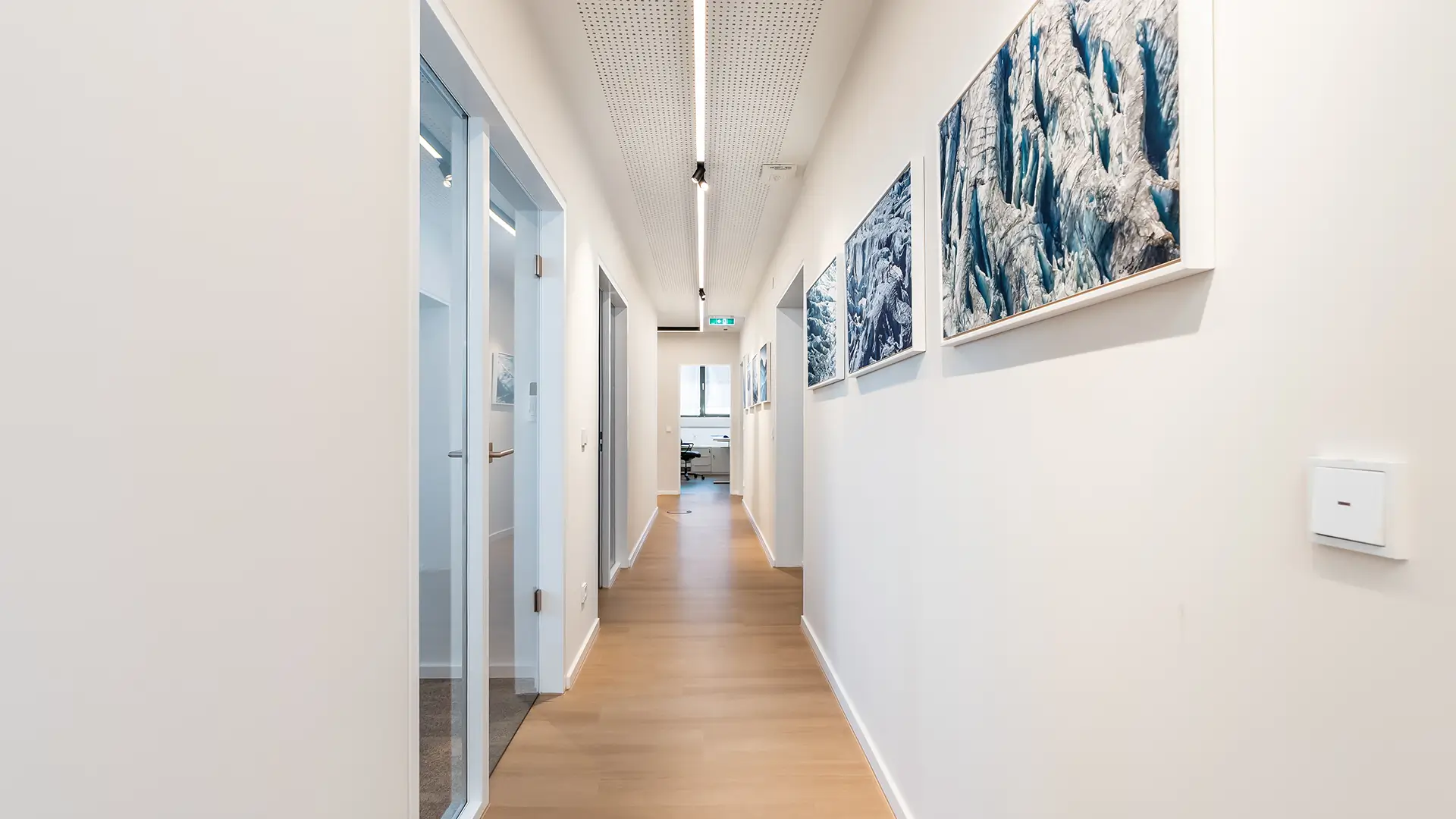 Heller Flur der Kanzlei mit modernen Glastüren und großformatigen Kunstwerken an den Wänden.