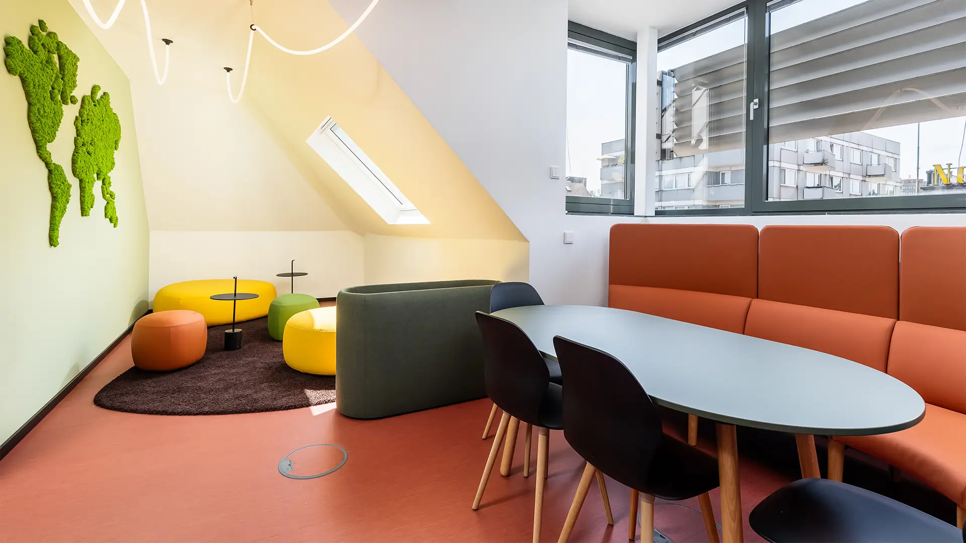 Gemütlicher Besprechungs- und Loungebereich mit Sitznischen, Besprechungstisch und dekorativer Pflanzenwand.