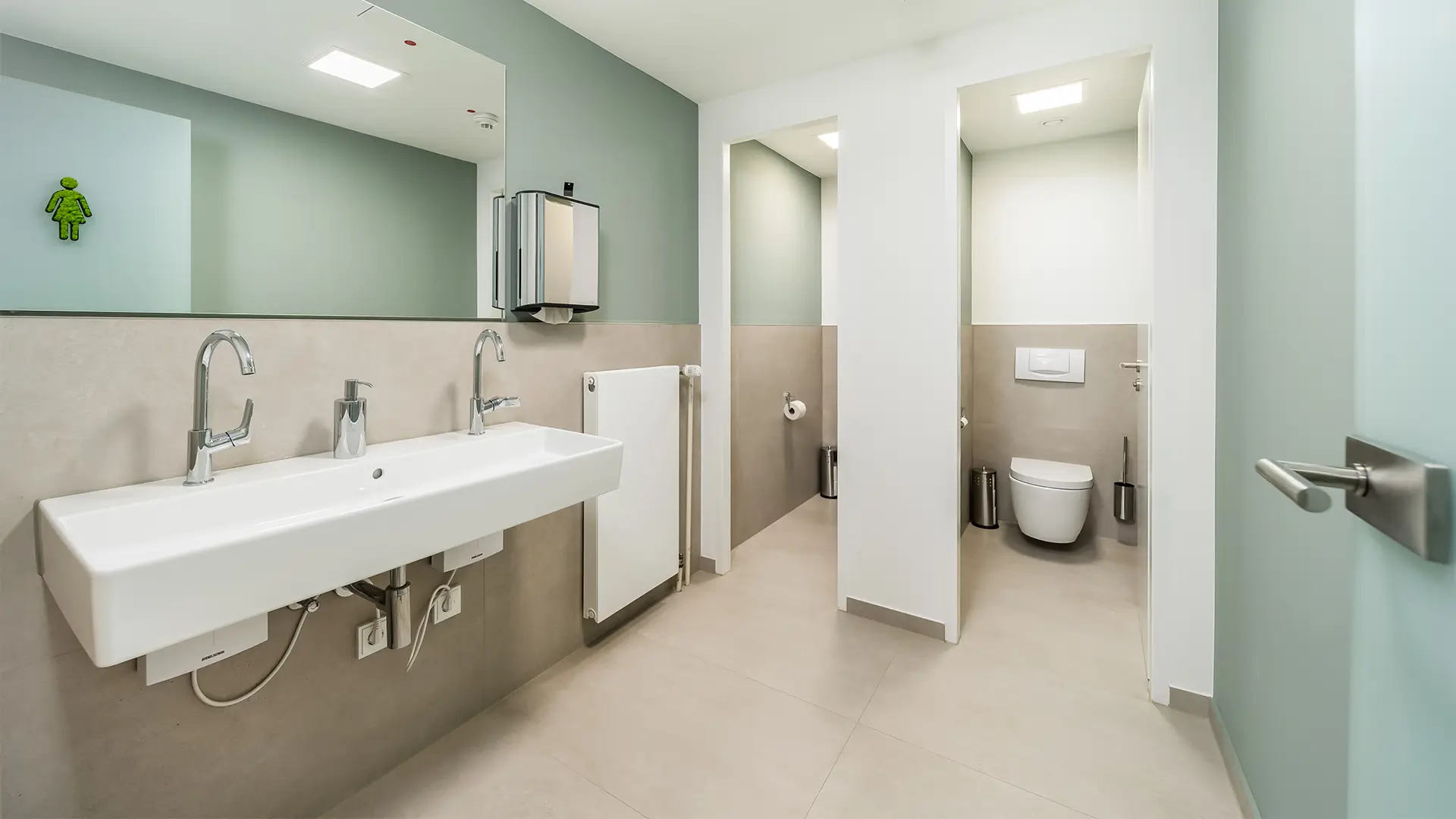 Modern ausgestatteter Sanitärbereich mit Doppelwaschbecken, separaten Toiletten und heller Gestaltung.