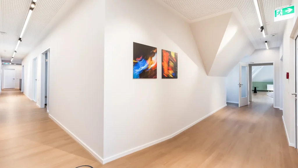 Heller Flurbereich mit moderner Beleuchtung, Kunstwerken und Zugang zu den Büroräumen.